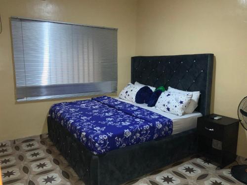 a bedroom with a bed with a blue comforter and a window at Charlies 2 Bedroom Apartment Ikeja in Ikeja