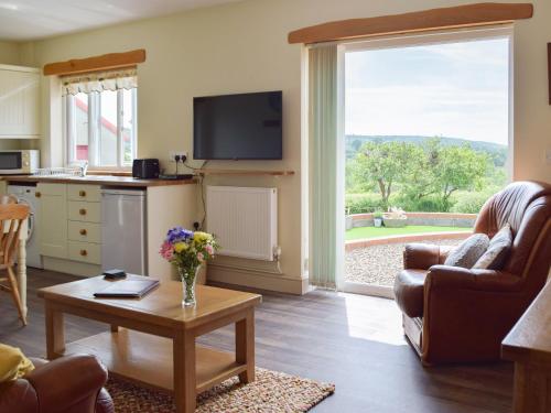 a living room with a table and a kitchen with a window at Piglets Cottage in Robeston Wathen