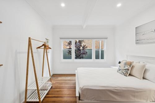 Un dormitorio blanco con una cama y una ventana. en Seabreeze - Macauley's Retro Beachside Vibes, en Coffs Harbour