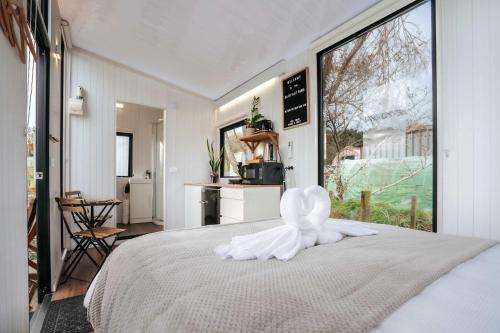 a bedroom with a white bed with a large window at Kiwi Farm Cabin 1 by Tiny Away in Waitoki