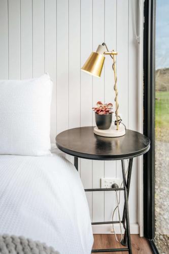 a table with a lamp on it next to a bed at Kiwi Farm Cabin 1 by Tiny Away in Waitoki