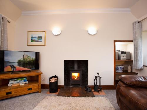a living room with a fireplace and a television at Craigellachie Cottage in Croy