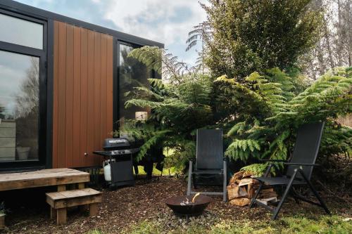 a house with two chairs and a tree at Kiwi Farm Cabin 2 by Tiny Away in Waitoki