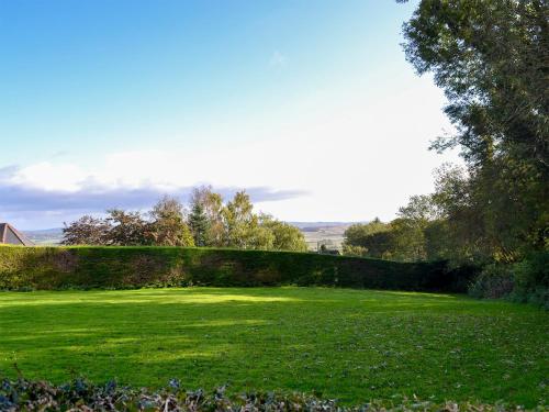 a green lawn with a hedge and trees in the background at Butterhole Farmhouse in Kelton