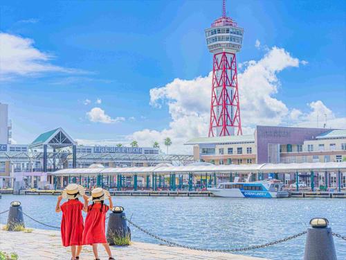 two women in red dresses standing near the water with a lighthouse at Tokyu Stay Hakata in Fukuoka