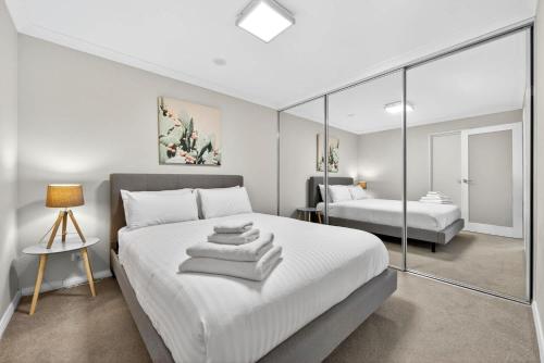 a white bedroom with two beds and a mirror at Stylish Rockingham Getaway 2BR Coastal Apartment in Rockingham