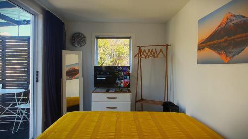 a bedroom with a yellow bed and a television at Cozy Tiny House Near The Beach in New Plymouth