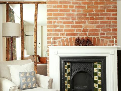 a living room with a brick wall and a fireplace at Pilgrim Cottage in Hollingbourne