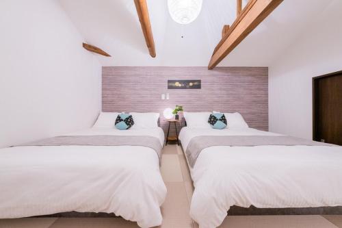 two beds in a room with white walls and wooden ceilings at 光 和風お風呂を楽しむお宿 usjまで電車で1分 駐車場付き ベッド6台 寝室3つ バスルーム2台 in Osaka