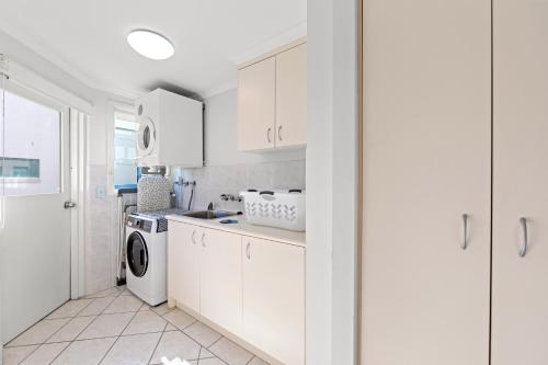 a kitchen with white cabinets and a washer and dryer at Alexandra on the Pacific in Mooloolaba