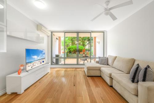 a white living room with a couch and a tv at Redfern 2Br Near CBD Shopping Center with Pool & Gym in Sydney