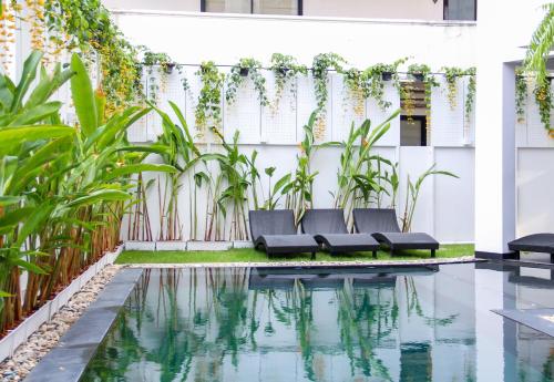 ein Pool mit zwei schwarzen Bänken neben einer weißen Wand mit Pflanzen in der Unterkunft iThaphae Hotel in Chiang Mai