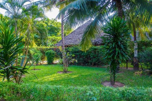 a tropical garden with palm trees and a hut at Lannan Escapes in Diani Beach