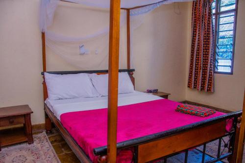 a bedroom with a four poster bed with a pink blanket at Lannan Escapes in Diani Beach