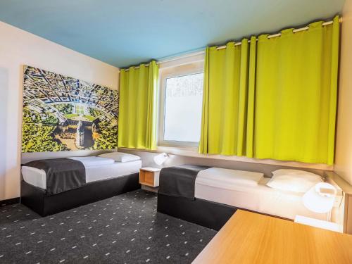 two beds in a room with yellow curtains at B&B Hotel Karlsruhe in Karlsruhe
