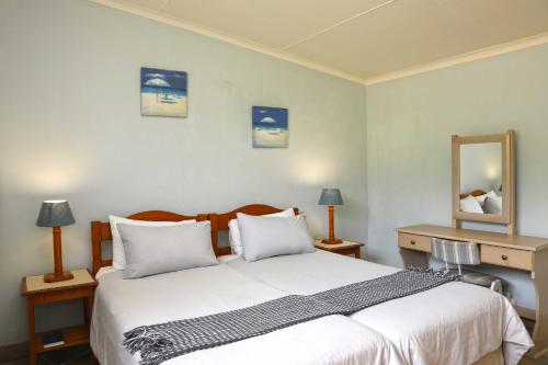 a bedroom with a bed with white sheets and a mirror at Neptunes Cove in Kei-mouth Village