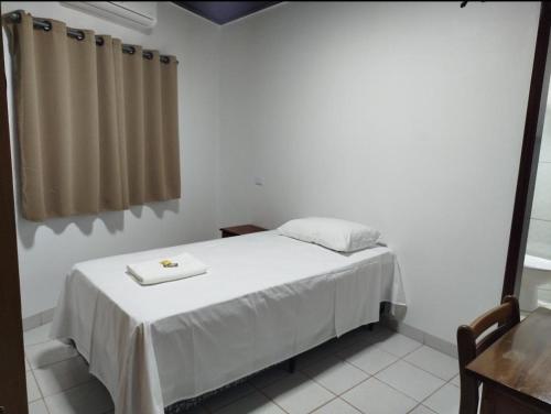 a bedroom with a bed with a table and a window at Hotel Maringá in Juara