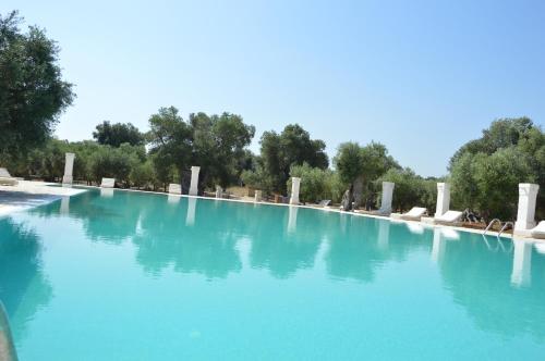 a large pool of blue water with chairs and trees at Agriturismo Masseria San Leonardo in Savelletri di Fasano