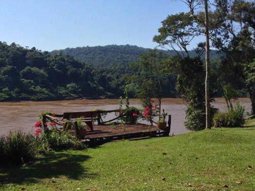 a bench sitting next to a river with flowers at La Mision Mocona - Lodge de Selva in Saltos del Moconá