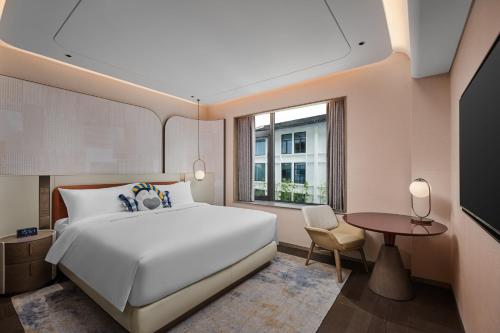 a bedroom with a large white bed and a table at voco Xitang by IHG in Jiaxing