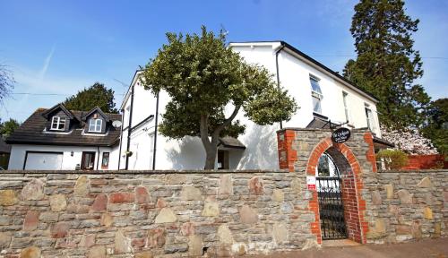 a white house behind a stone wall with a tree at The Lychgate in Caldicot