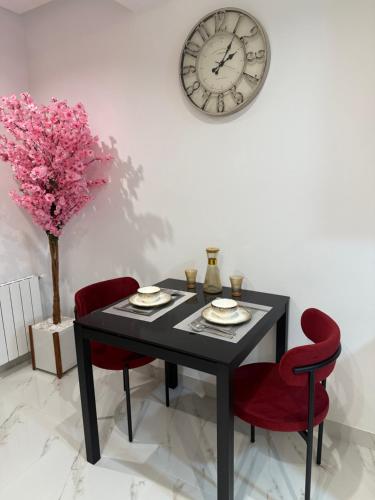 Una mesa de comedor con dos sillas rojas y un reloj. en appartement A33, en Burj at Turkī