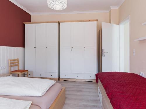 a bedroom with white cabinets and a red bed at Cozy Escape Near the Baltic in Gingst