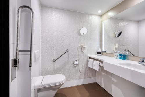 a white bathroom with a toilet and a sink at Crowne Plaza Hotel Brugge by IHG in Bruges