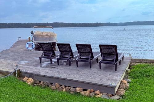 a dock with four chairs and a boat on the water at Lakefront Home with Hot Tub and Dock in Cross Hill! in Cross Hill