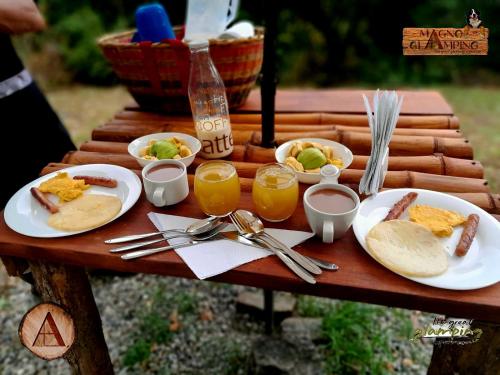 a table with plates of food and glasses of orange juice at Magno Glamping Combita in Cómbita