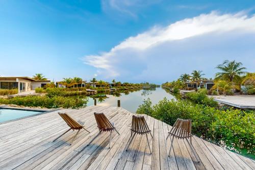 three chairs sitting on a wooden deck next to a body of water at Seabird Villa 11 in Placencia Village
