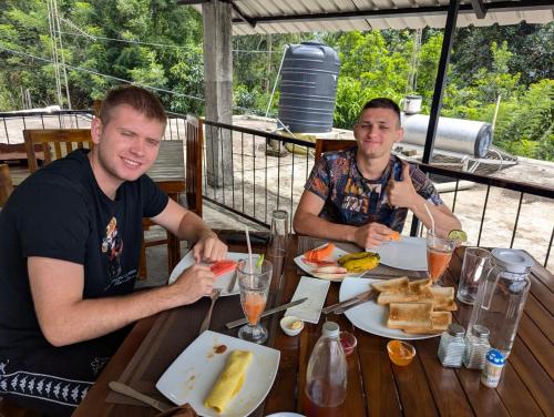 two men sitting at a wooden table eating food at Su Casa Ella in Ella