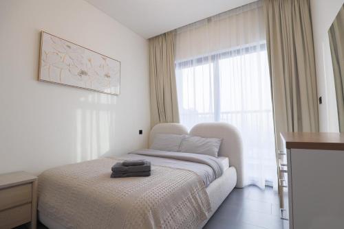a white bedroom with a bed and a window at Gracious 1BR in The Crest, Sobha Hartland in Dubai