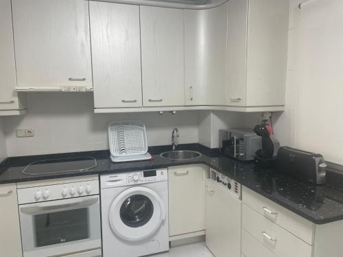 a kitchen with white cabinets and a washing machine at Céntrico, primera línea de playa y piscina in Laredo
