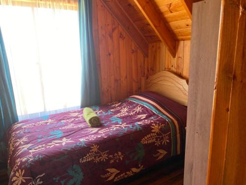 a small bed in a cabin with a purple comforter at Cabañas Santa María in Pichilemu