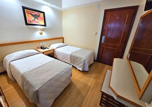 a hotel room with two beds and a door at Riale Imperial Flamengo in Rio de Janeiro