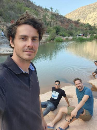 three men sitting on the shore of a body of water at hostel SmiGle in Tamraght Oufella