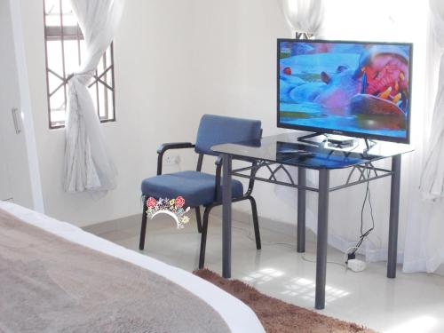 Schlafzimmer mit einem Schreibtisch, einem TV und einem Stuhl in der Unterkunft Twinhome Inn in Gaborone
