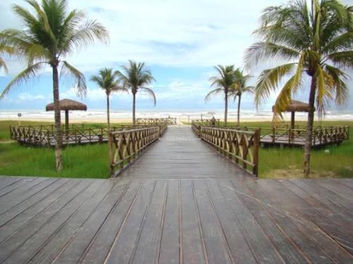 a wooden boardwalk leading to the beach with palm trees at Casa aconchegante em Aracaju na Aruana in Aracaju