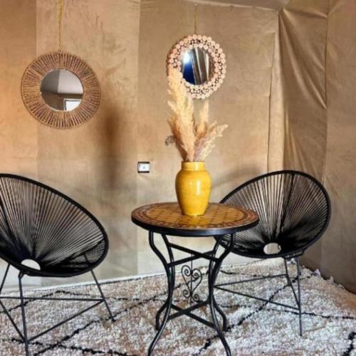 two chairs and a table with a vase on it at Merzouga traditional Camp in Merzouga