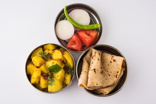 プネにあるCollection O Rajdhani Hotelのテーブルの上には、異なる種類の食べ物が入った4つの容器がある