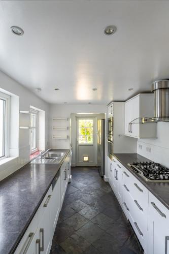 a large kitchen with white cabinets and a sink at Charming 3BR Victorian House with Parking - 10 Mins to Kingston in Kingston upon Thames
