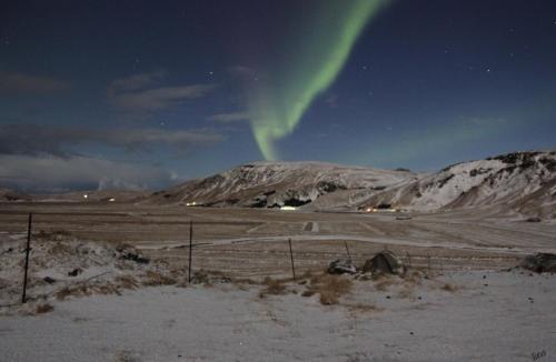 an aurora in the sky over a snowy field at Skammidalur cottages in Vík
