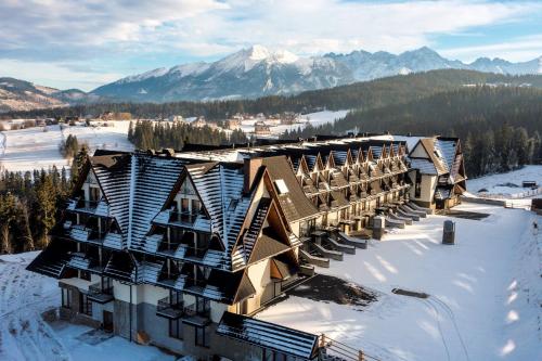 a resort in the snow with mountains in the background at Grand Stasinda Bal Sylwestrowy Animacje Impreza Integracyjna Dwa Posiłki Bogaty Bufet Baseny Kręgielnia Grota Sauny Squash Siłownia Place Zabaw Widoki 1000mnpm in Bukowina Tatrzańska