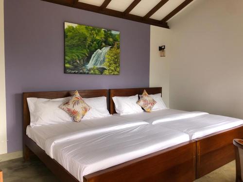 a bed in a bedroom with a waterfall painting on the wall at PEKOE VALLEY Huluganga in Huluganga
