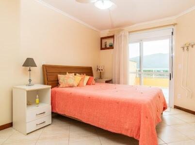 a bedroom with a bed with a orange bedspread and a window at Cobertura com piscina e vista da Lagoa da Conceição in Florianópolis