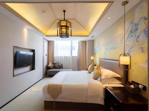 a bedroom with a large bed and a tv at Yuan Culture Hotel Shenzhen World Shajing in Shenzhen