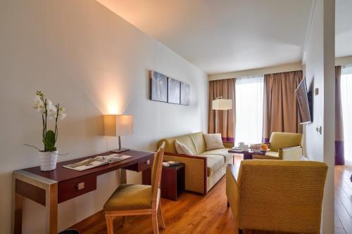 a living room with a couch and a desk in a room at Clarion Paris CDG Airport in Roissy-en-France