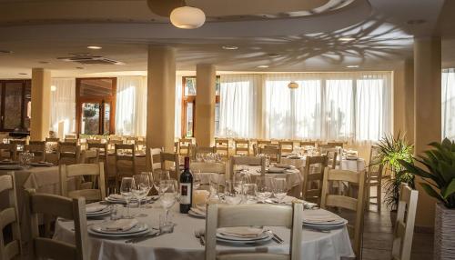 a dining room with white tables and chairs with wine bottles at Hotel Raffael PHG in Putzu Idu