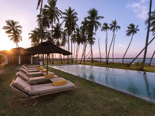 a group of lounge chairs next to a pool with palm trees at Jetwing Kottukal Beach House in Arugam Bay